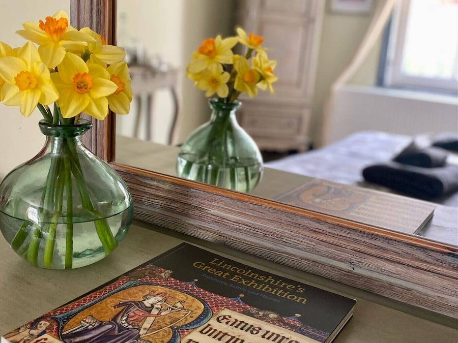 Een boek met de titel 'Lincolnshire's Great Exhibition' op een tafel, met twee glazen vazen vol narcissen.