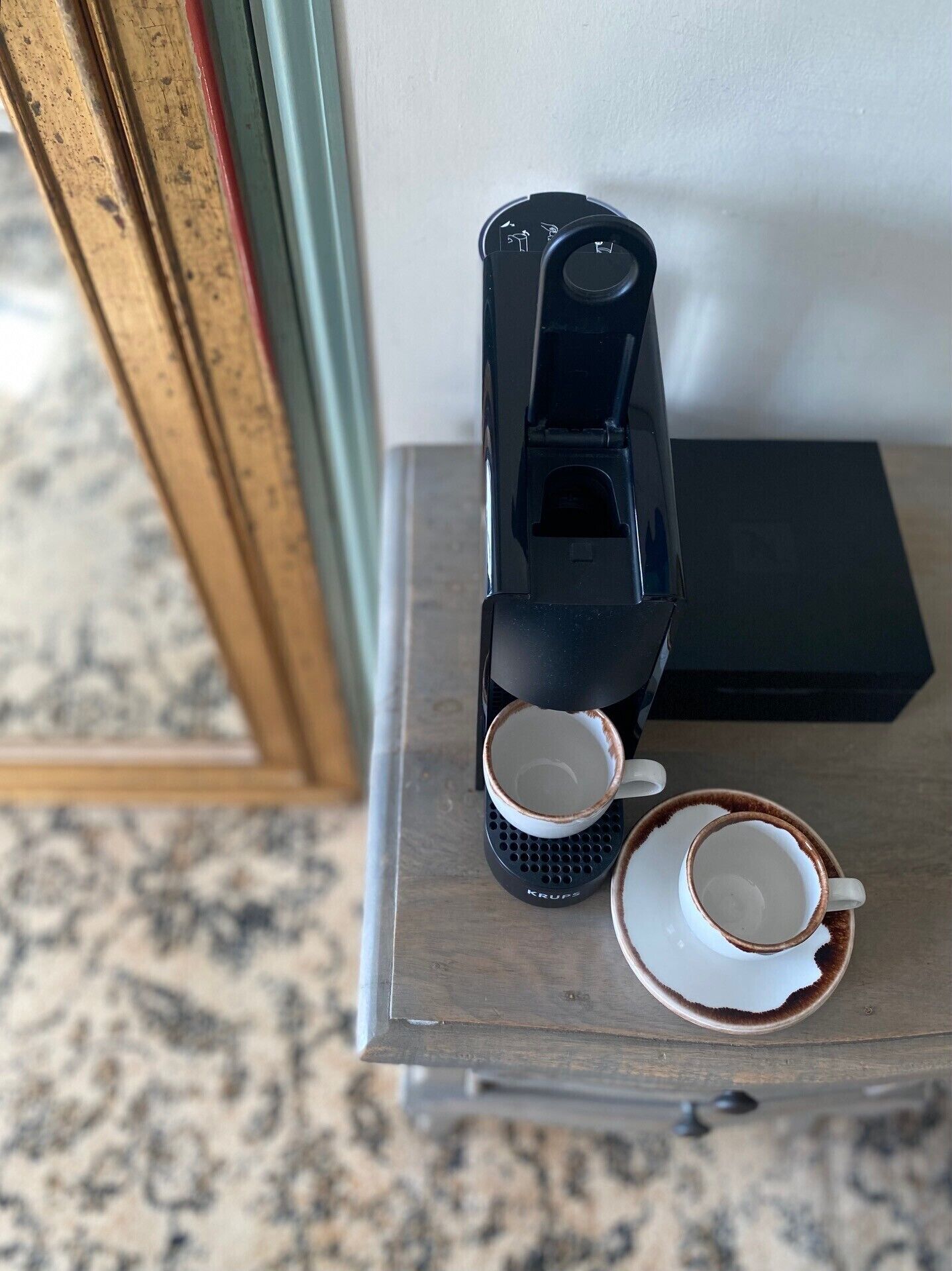 Una cafetera sobre una mesita con dos tazas, una negra y otra blanca con detalles marrones.