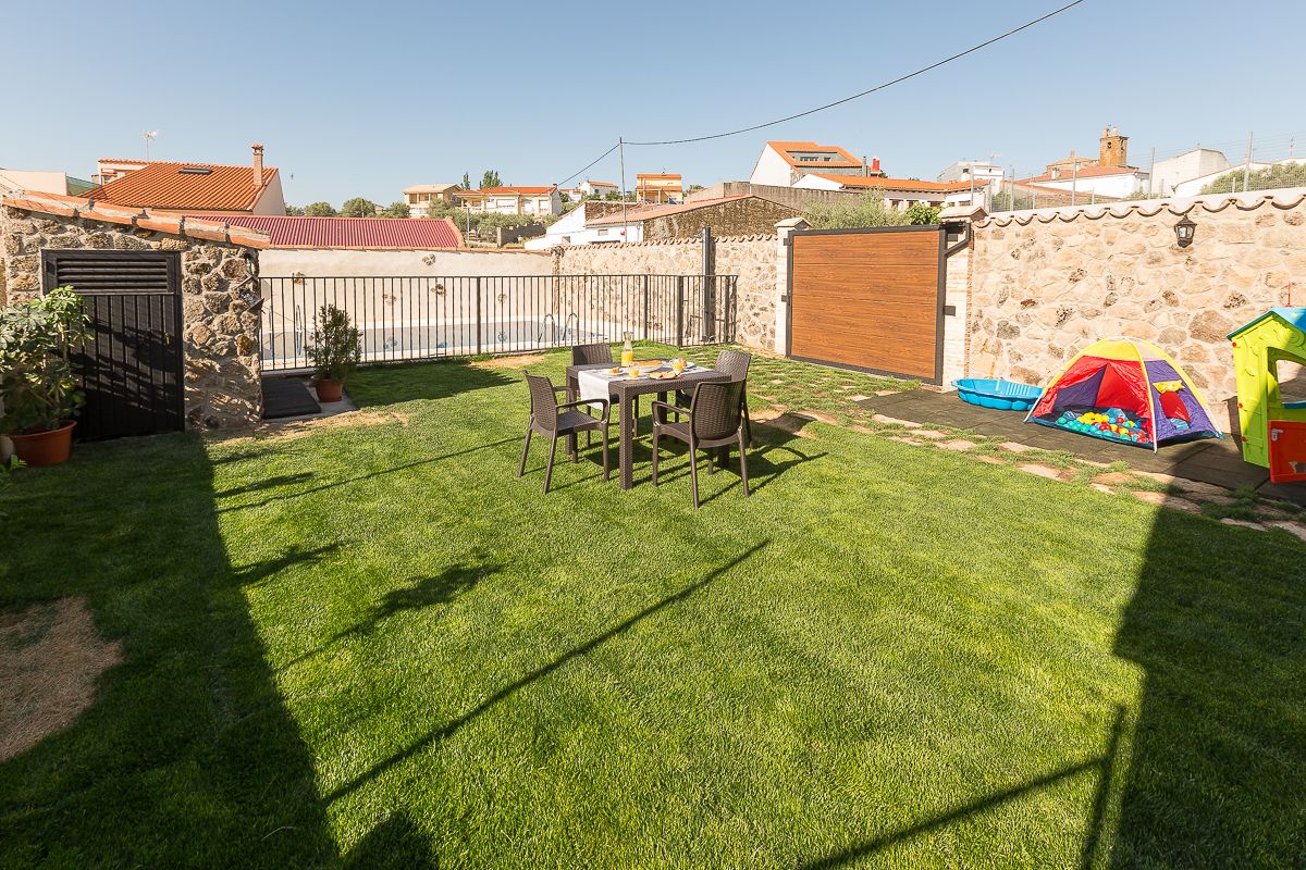 Un patio trasero con una mesa y sillas, una carpa infantil y un muro de piedra.