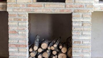 Een buitenoven van baksteen met een houtopslag eronder.