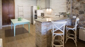 A kitchen with a central island, two bar stools, a wooden table with a plant, and a stone accent wall.