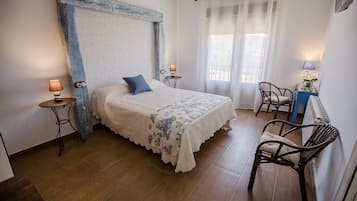 Quarto com cama grande, duas mesinhas de cabeceira, uma cadeira e janela com cortinas.