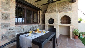 An outdoor patio with a stone wall, a brick oven, and a table set for breakfast.
