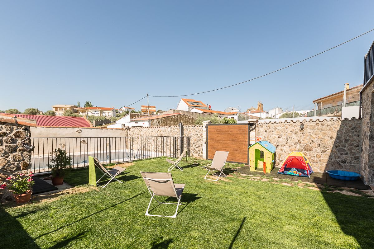 Un patio trasero con un muro de piedra, una casita de juegos, una carpa y dos sillas de jardín.
