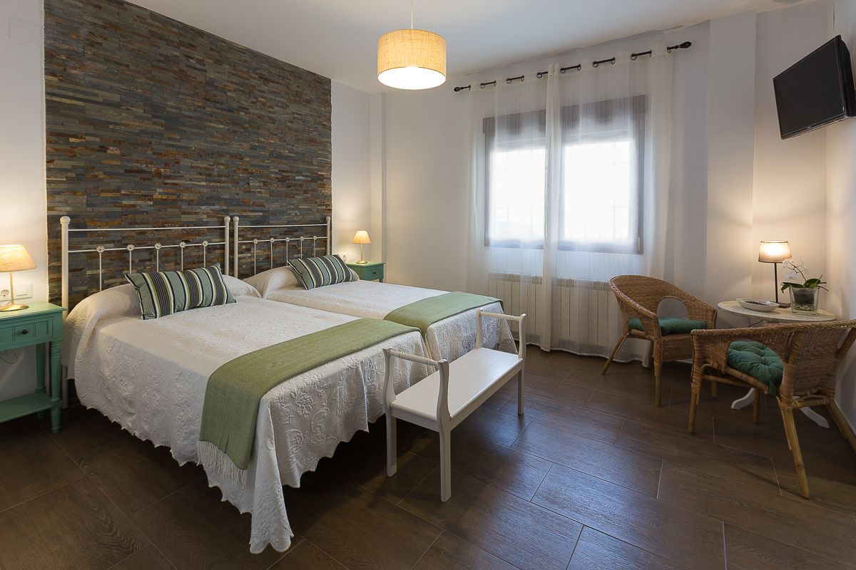 Une chambre avec deux lits, un mur décoratif en briques, une télévision et une petite table avec une chaise.