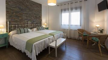 Une chambre avec deux lits, un mur décoratif en briques, une télévision et une petite table avec une chaise.