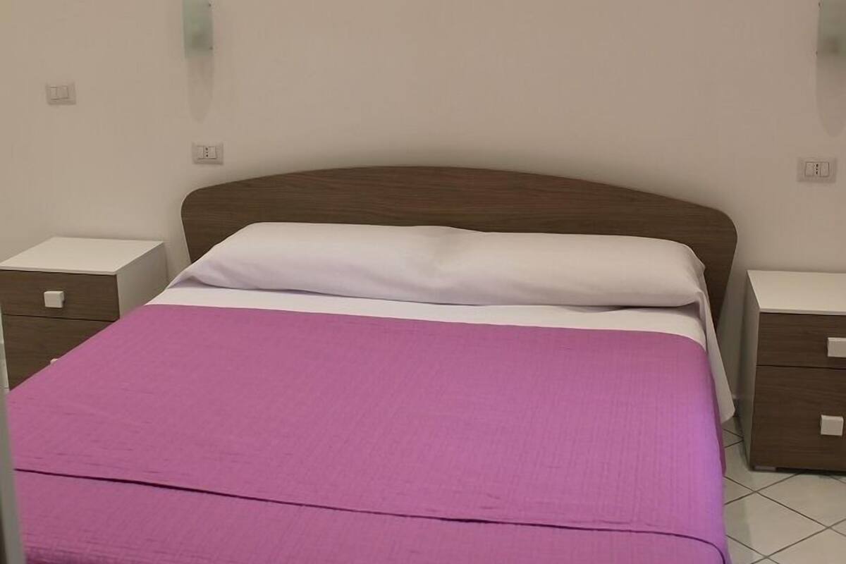A single bed with a wooden headboard, a purple bedspread, and two bedside tables with drawers.
