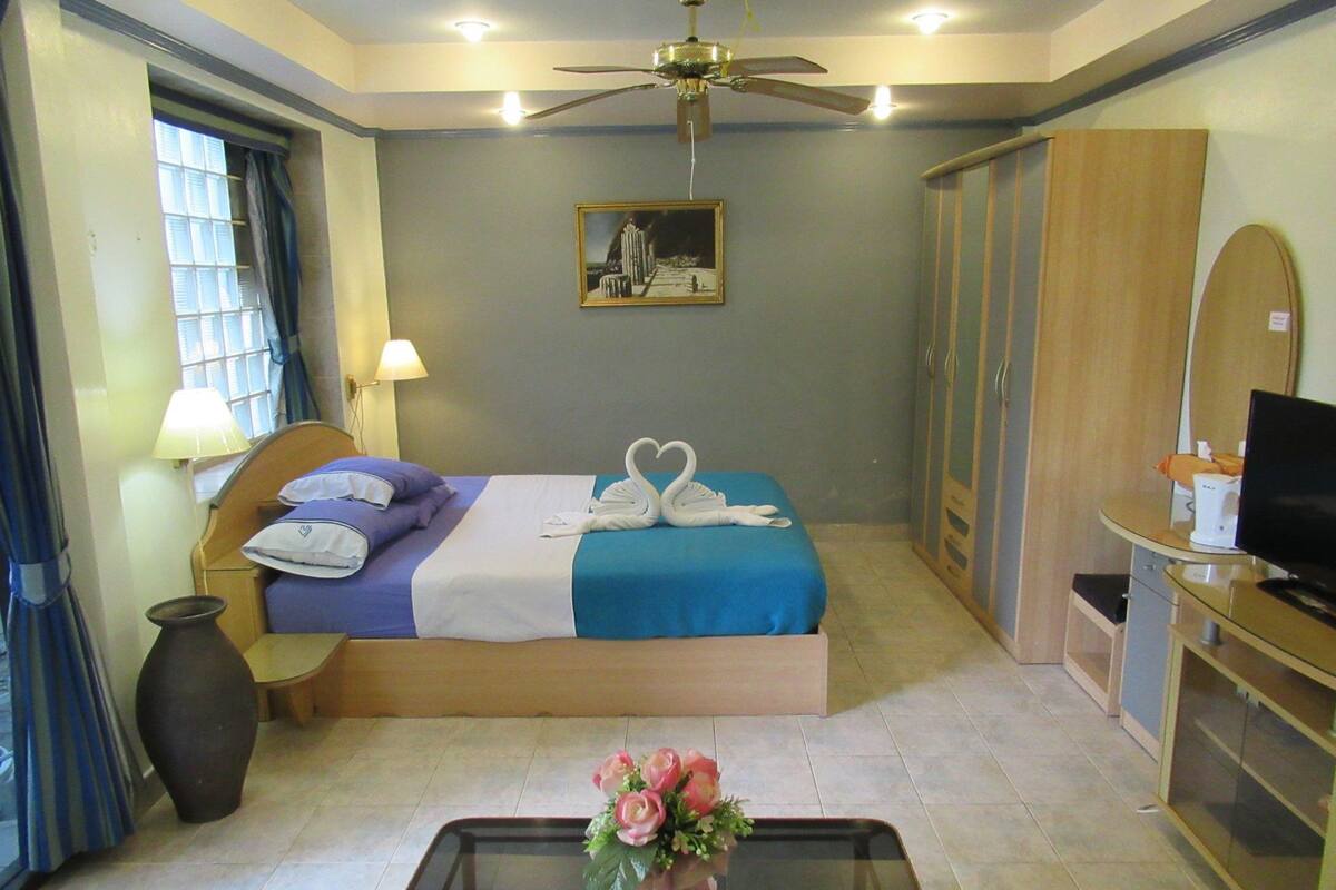 A hotel room with a bed, a desk, a television, a wardrobe, and a painting on the wall.