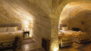 A cozy, cave-like bedroom with a bed, two bedside tables, and a small seating area. - Roca Cappadocia (Ürgüp)