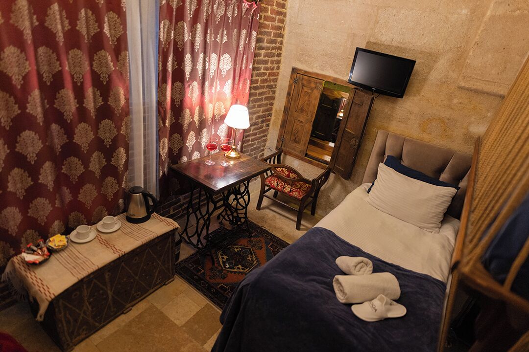 A hotel room with a bed, a desk with a lamp, a TV, and a small table with a coffee pot and glasses.