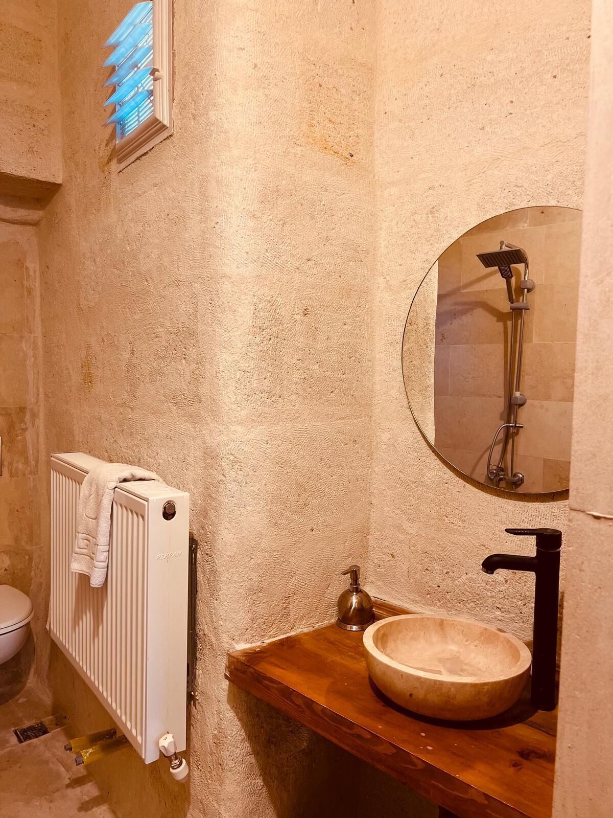 A bathroom with a wooden vanity, a round mirror, a shower, and a radiator.