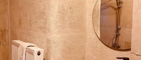 A bathroom with a wooden vanity, a round mirror, a shower, and a radiator.