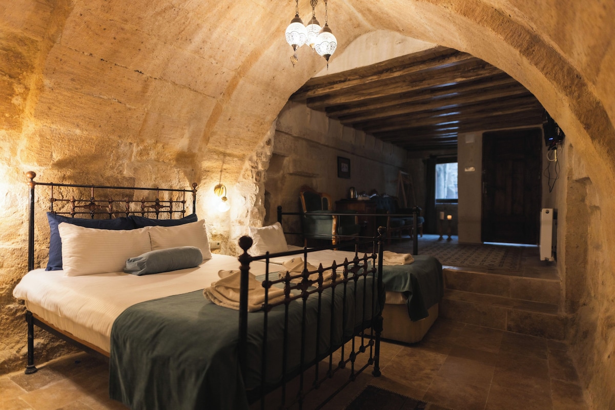 A stone-walled bedroom with a bed, a wooden ceiling, and a stone floor.