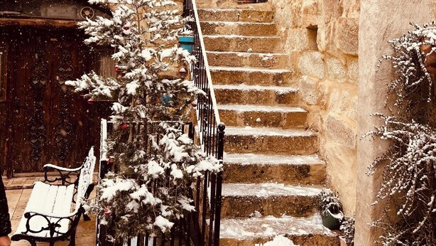 A snow-covered courtyard with stone steps, potted plants, and a bench. - Roca Cappadocia (Ürgüp)