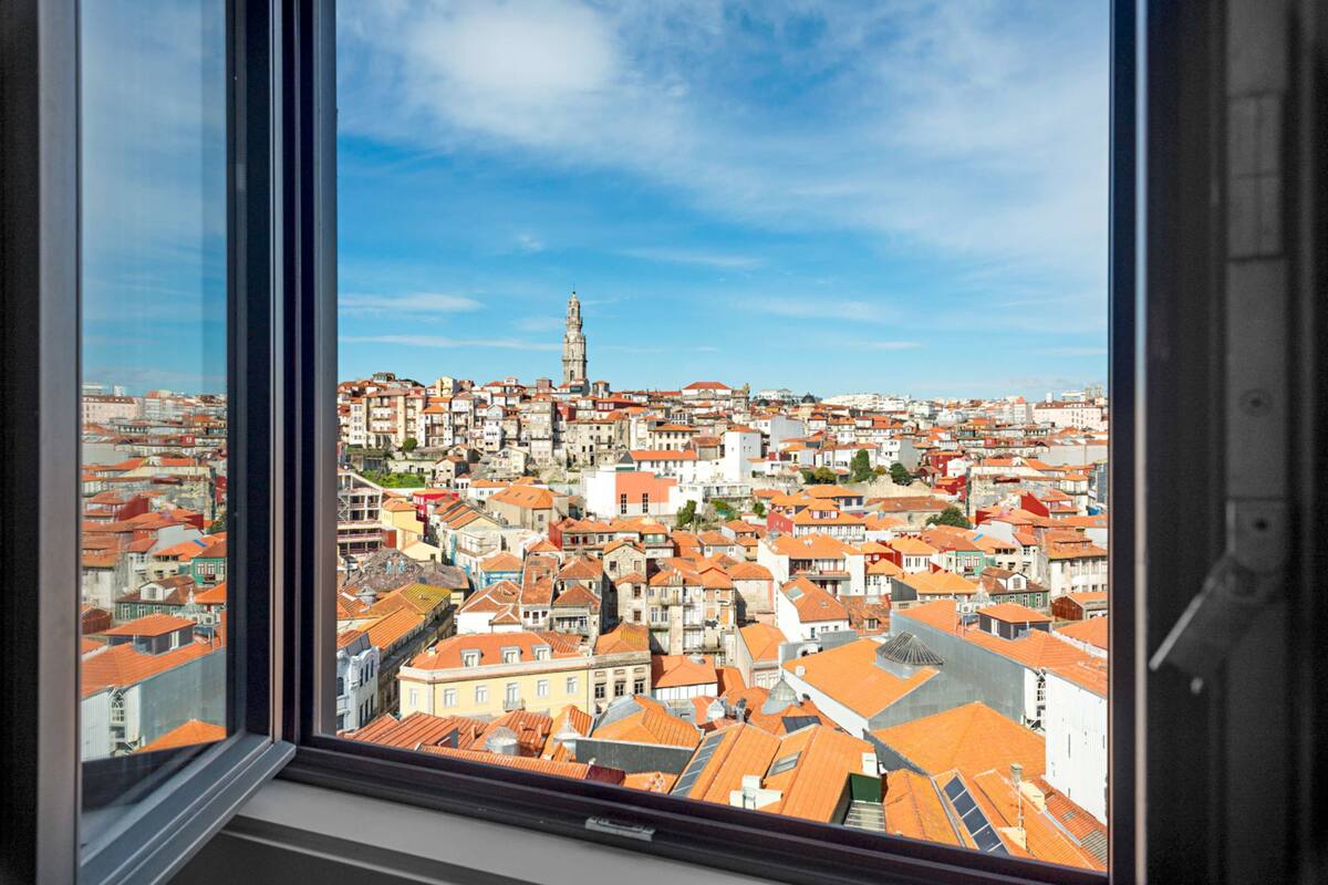A panoramic view of a cityscape through a window, featuring a prominent tower and densely packed buildings with red-tiled roofs.