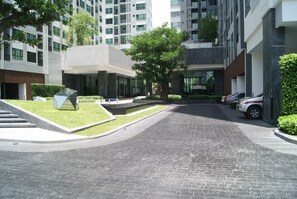 A modern building with a paved driveway, a glass atrium, and a parking area with cars.