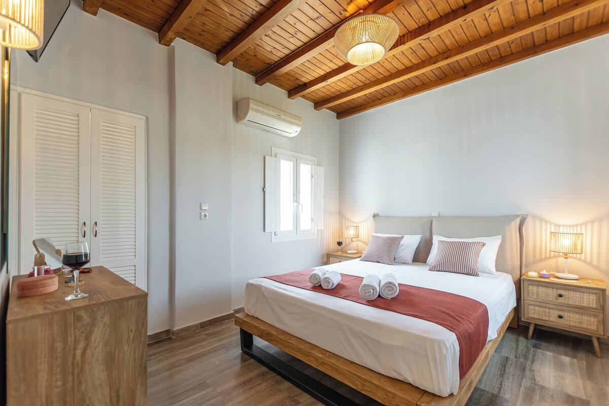 Un dormitorio con cama de madera, cortinas blancas, una mesita de noche con lámpara y suelo de madera.