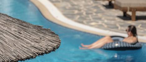 Una piscina con sillas de descanso y una sombrilla de paja.