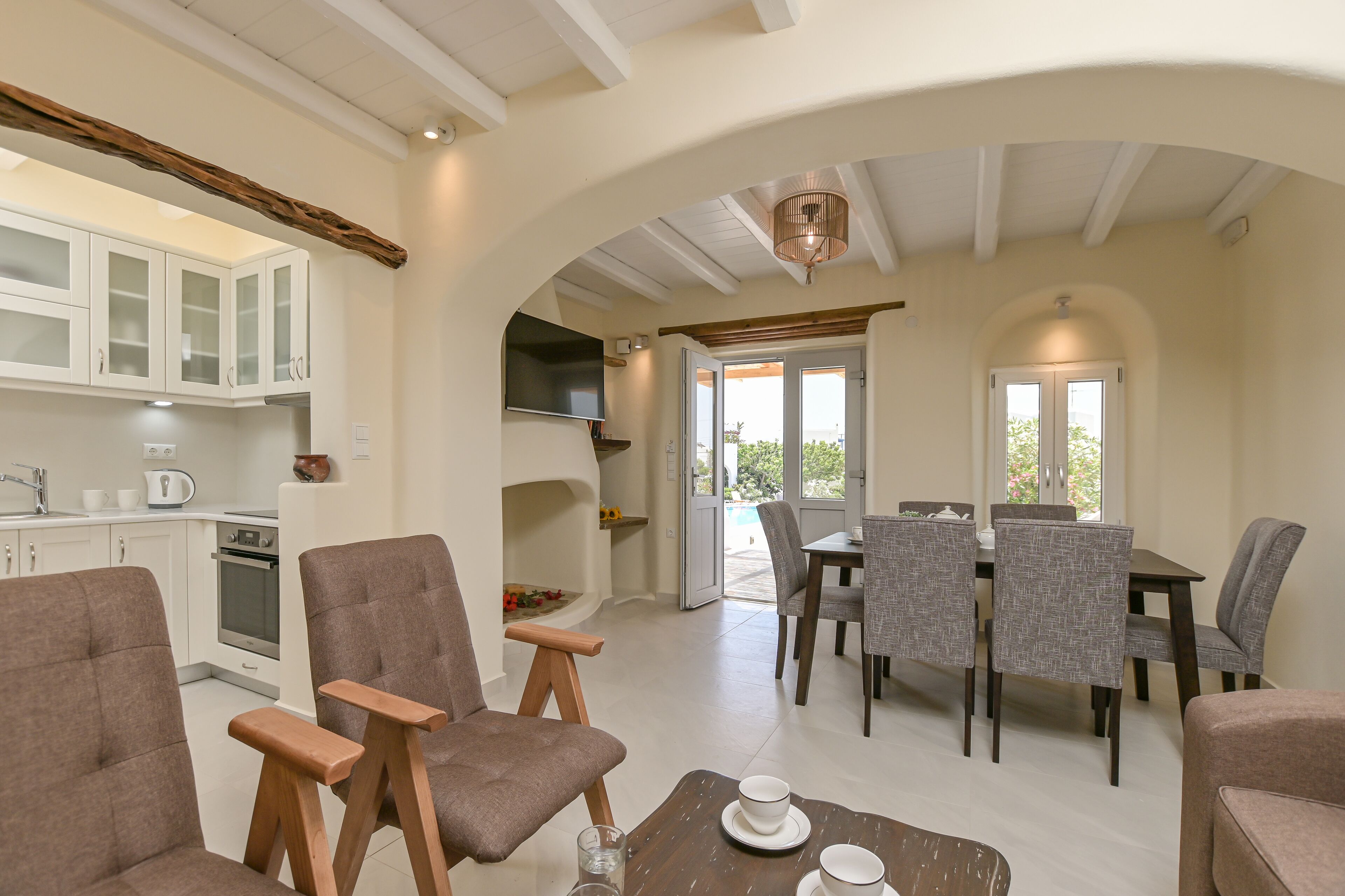 Amplia sala de estar con mesa de comedor, varias sillas, una cocina con armarios blancos y una chimenea.