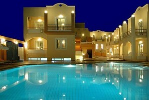 A multi-story hotel with a swimming pool, balconies, and warm lighting. - Nontas Hotel Apartaments (Chania)