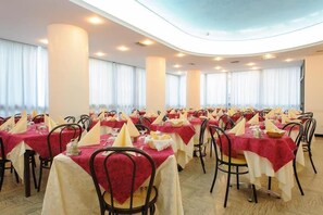 A banquet hall with round tables, chairs, and a high ceiling. - Christian Hotel (Riccione)