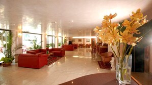 A spacious lobby with red sofas, a glass coffee table, and a vase of yellow orchids.