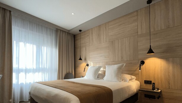 Ein modernes Hotelzimmer mit einem großen Bett, einem Nachttisch mit Lampe und einer Wand mit Holzverkleidung.