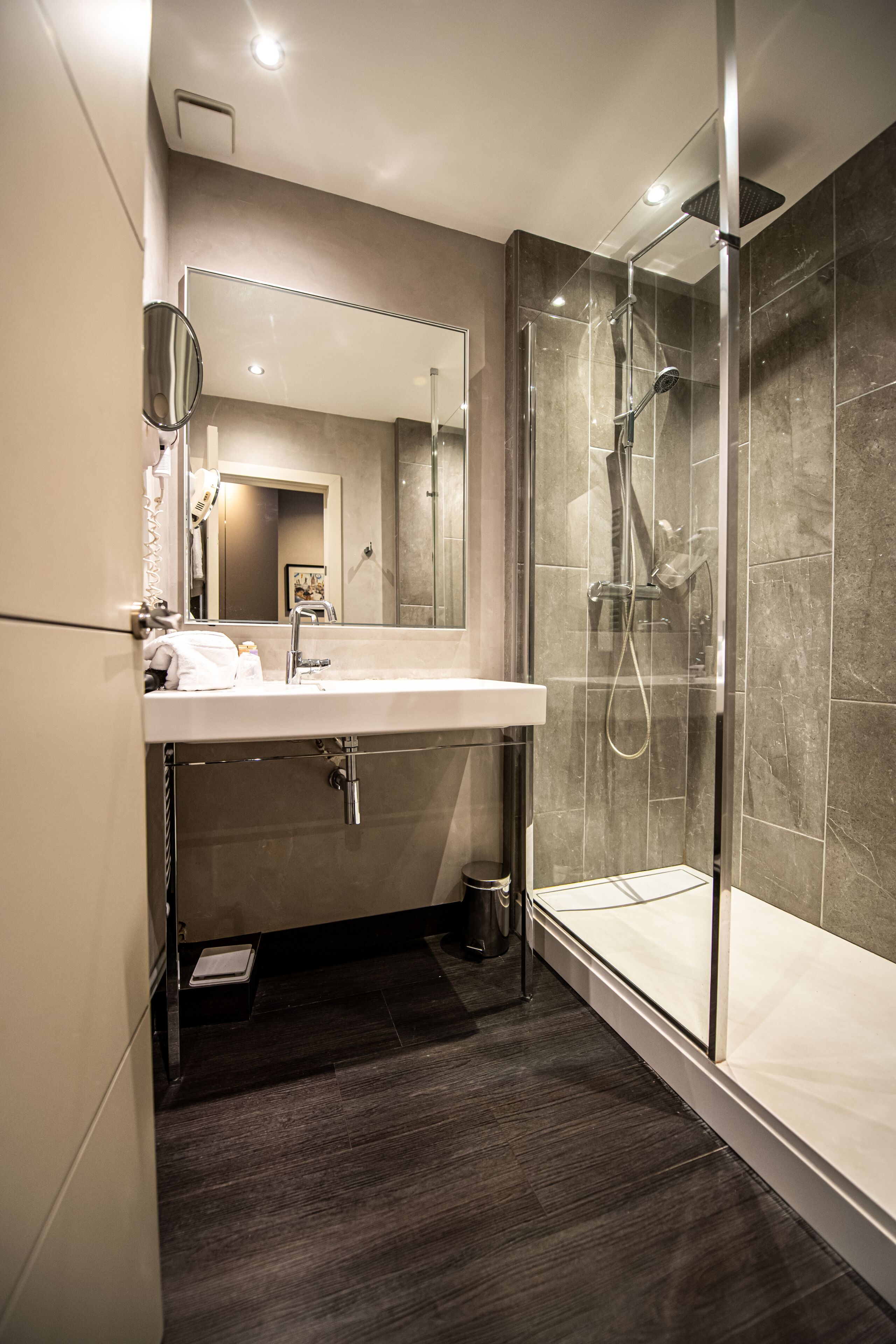 Un baño moderno con ducha de vidrio, un espejo grande y un lavamanos blanco.