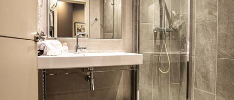 Un baño moderno con ducha de vidrio, un espejo grande y un lavamanos blanco.