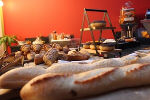 Variedad de panes y pasteles a la vista, incluyendo croissants y barras de pan, con una cafetera al fondo.