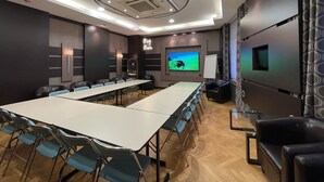 Ein Konferenzraum mit langem Tisch, Stühlen, einer Projektionsleinwand und einem Fernseher.