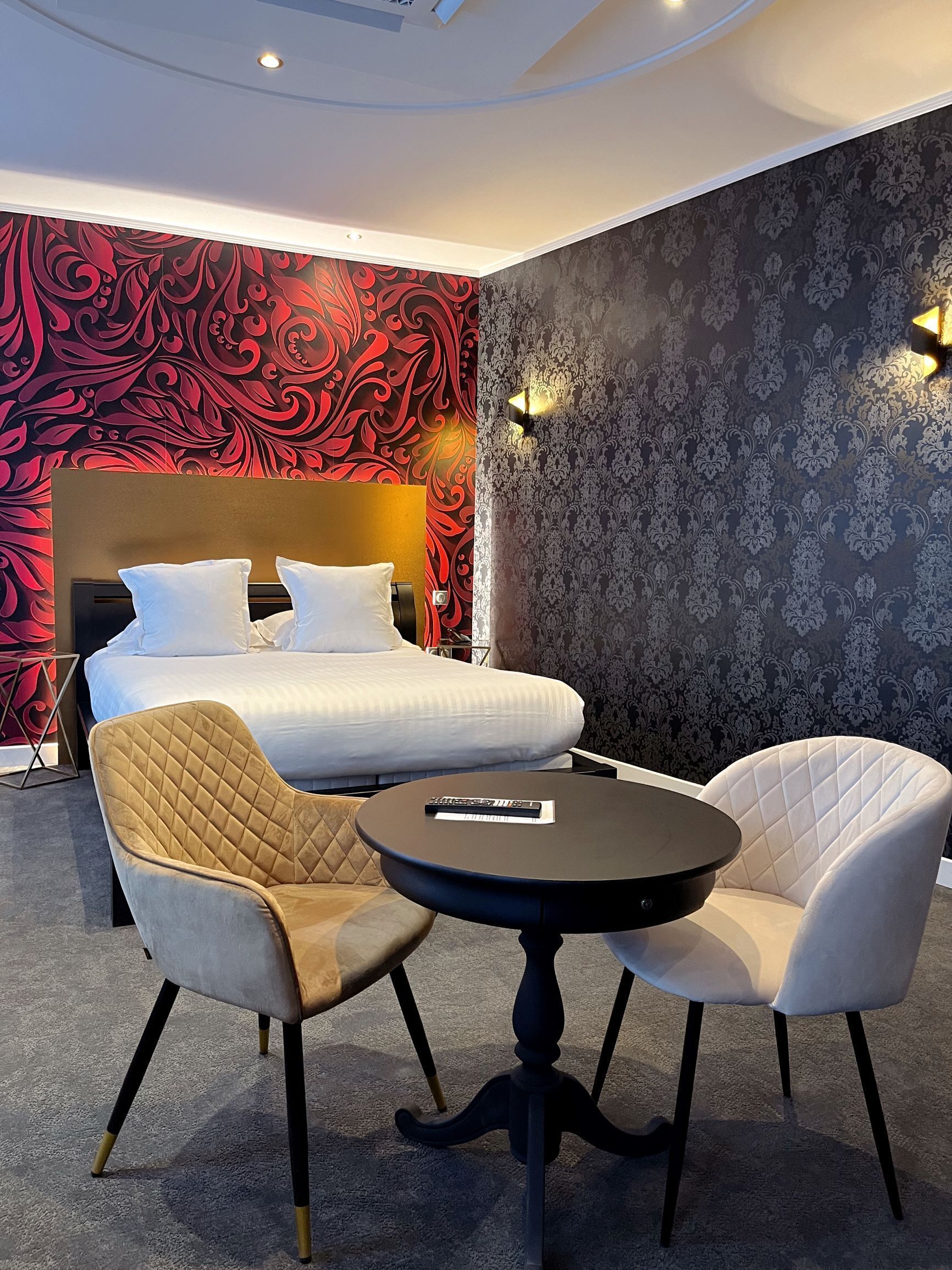 Une chambre d’hôtel avec un lit, deux chaises, une petite table et un mur décoratif.