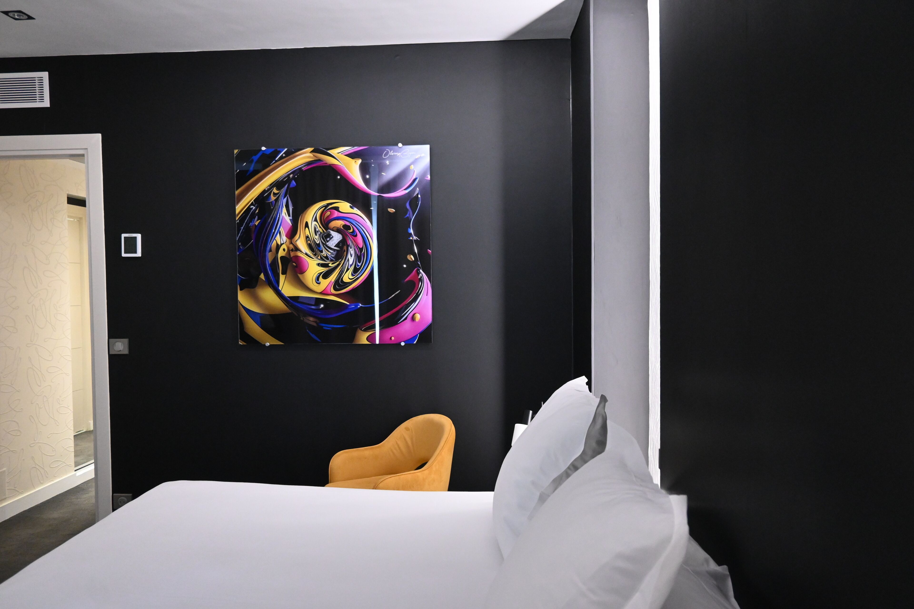 A hotel room with a large abstract painting on the wall, a bed with white linens, and a mustard-colored armchair.