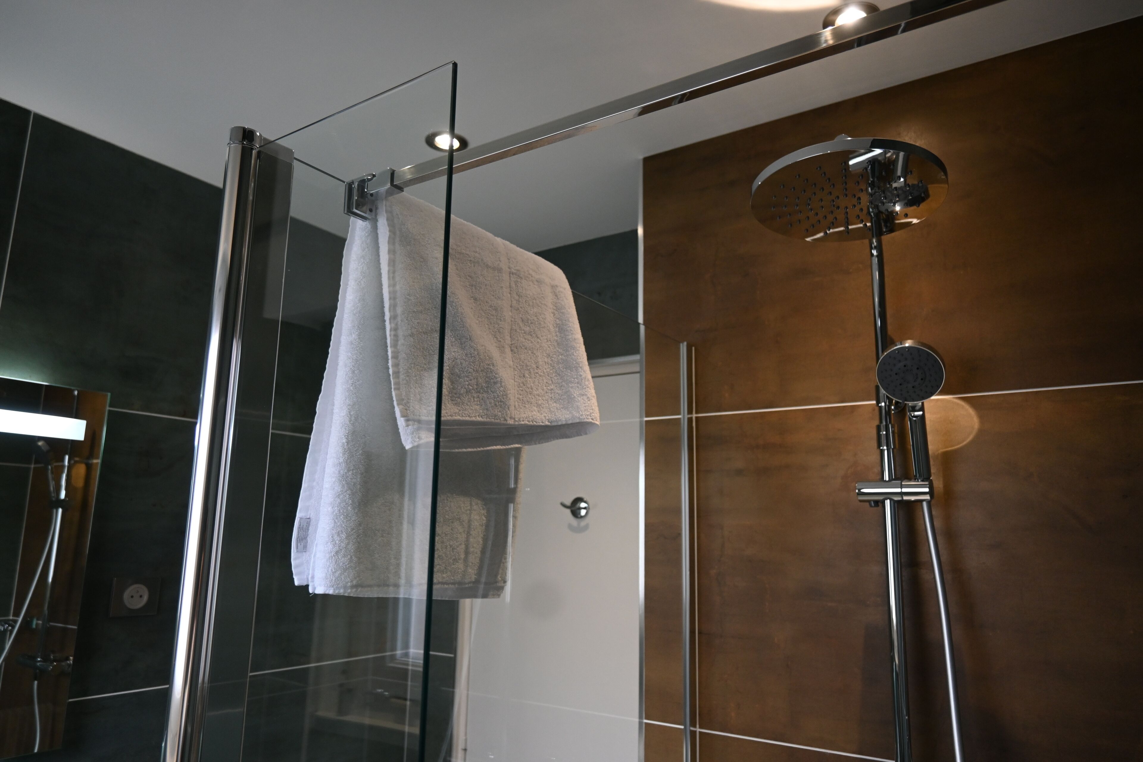A modern bathroom with a glass-enclosed shower, a handheld showerhead, and a towel hanging on a rack.