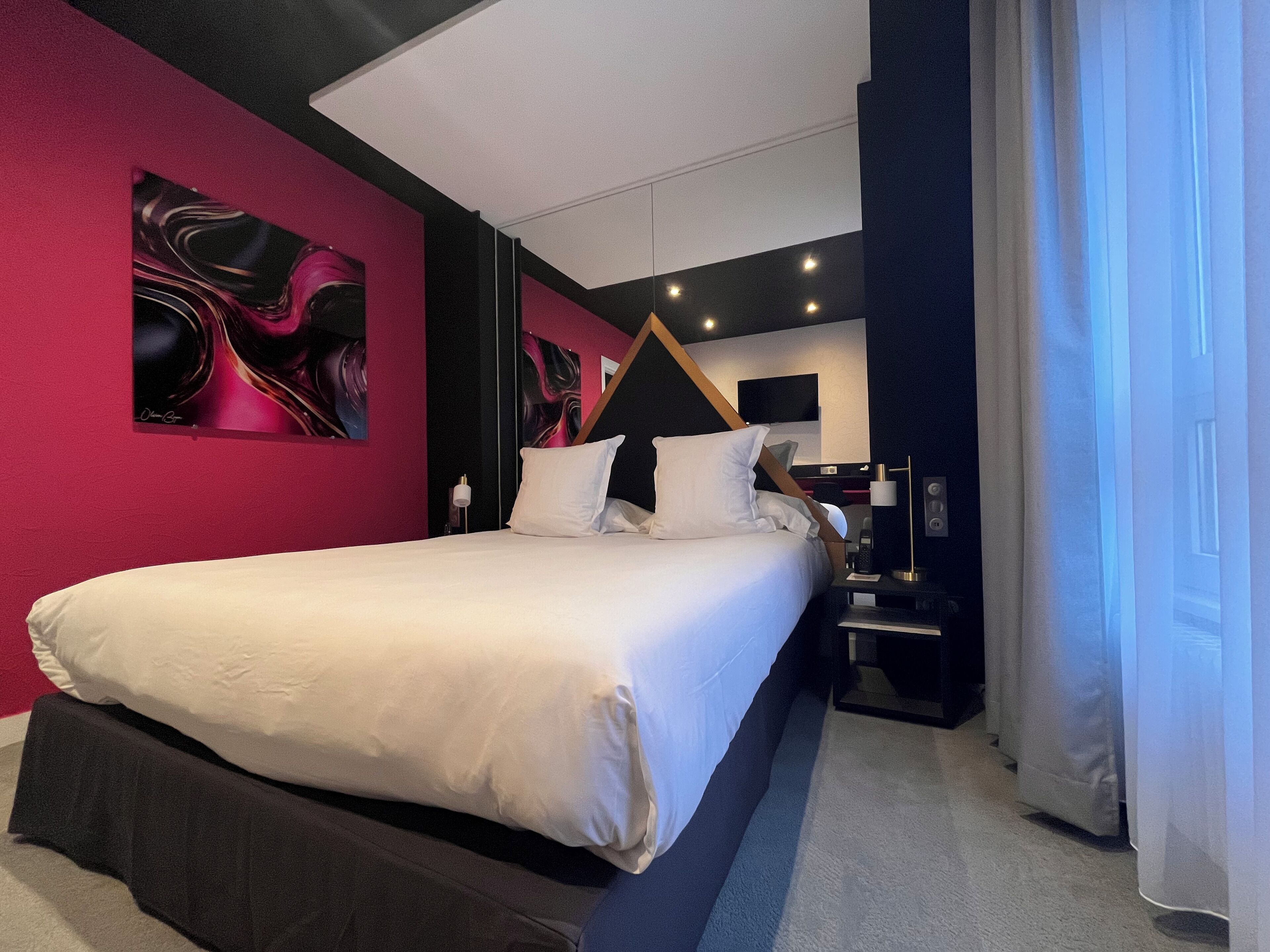 A modern hotel room with a large bed, a flat-screen TV, and a painting on the wall.