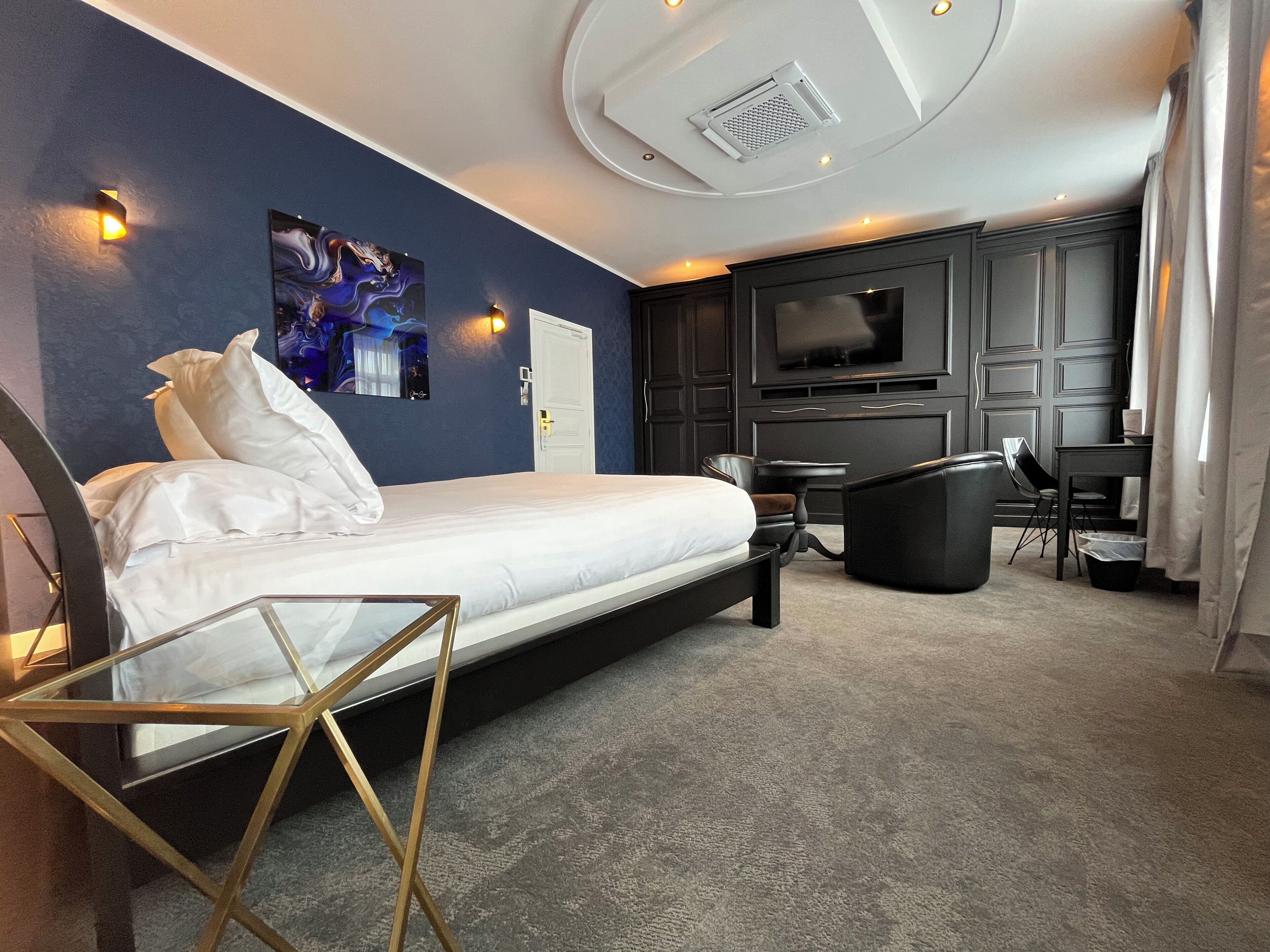 A modern hotel room with a bed, a desk, a chair, a TV, and a painting on the wall.