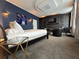 Habitación de hotel moderna con cama, escritorio, silla, televisor y un cuadro en la pared.