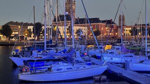 Eine Marina mit mehreren Segelbooten an den Liegen, ein markanter Turm im Hintergrund und Gebäude entlang des Ufers.