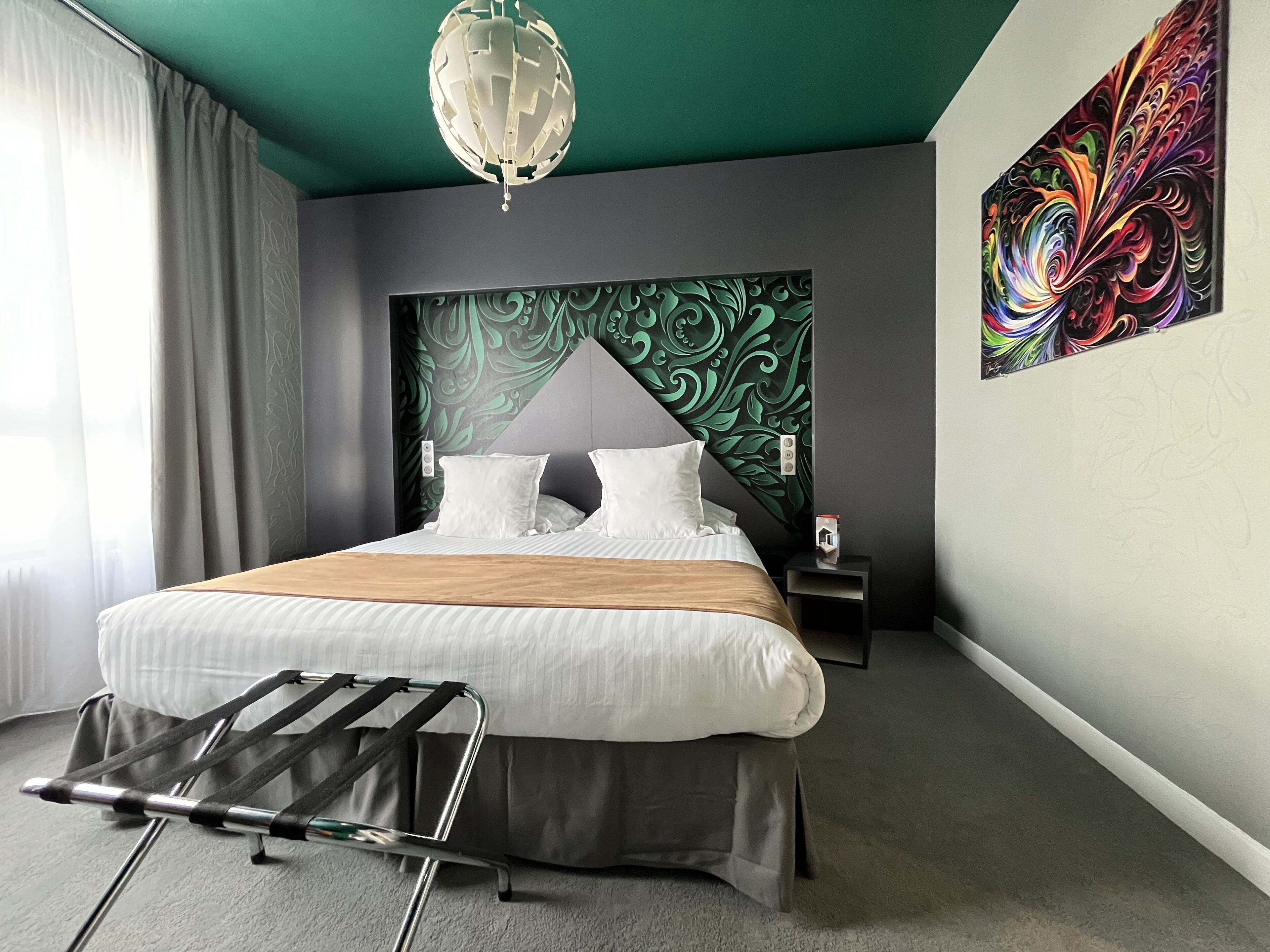 A modern hotel room with a large bed, a unique green accent wall, and a vibrant abstract painting.