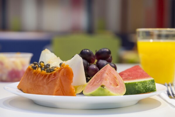 Un plato con diversas frutas y un vaso de jugo de naranja.