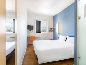 A hotel room with a bed, a desk, a chair, a TV, and a window with a city view. - ibis budget Curitiba Centro (Curitiba)