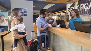 A reception area with a wooden counter, a Dell computer, and a child holding a toy. - ibis budget Curitiba Centro (Curitiba)