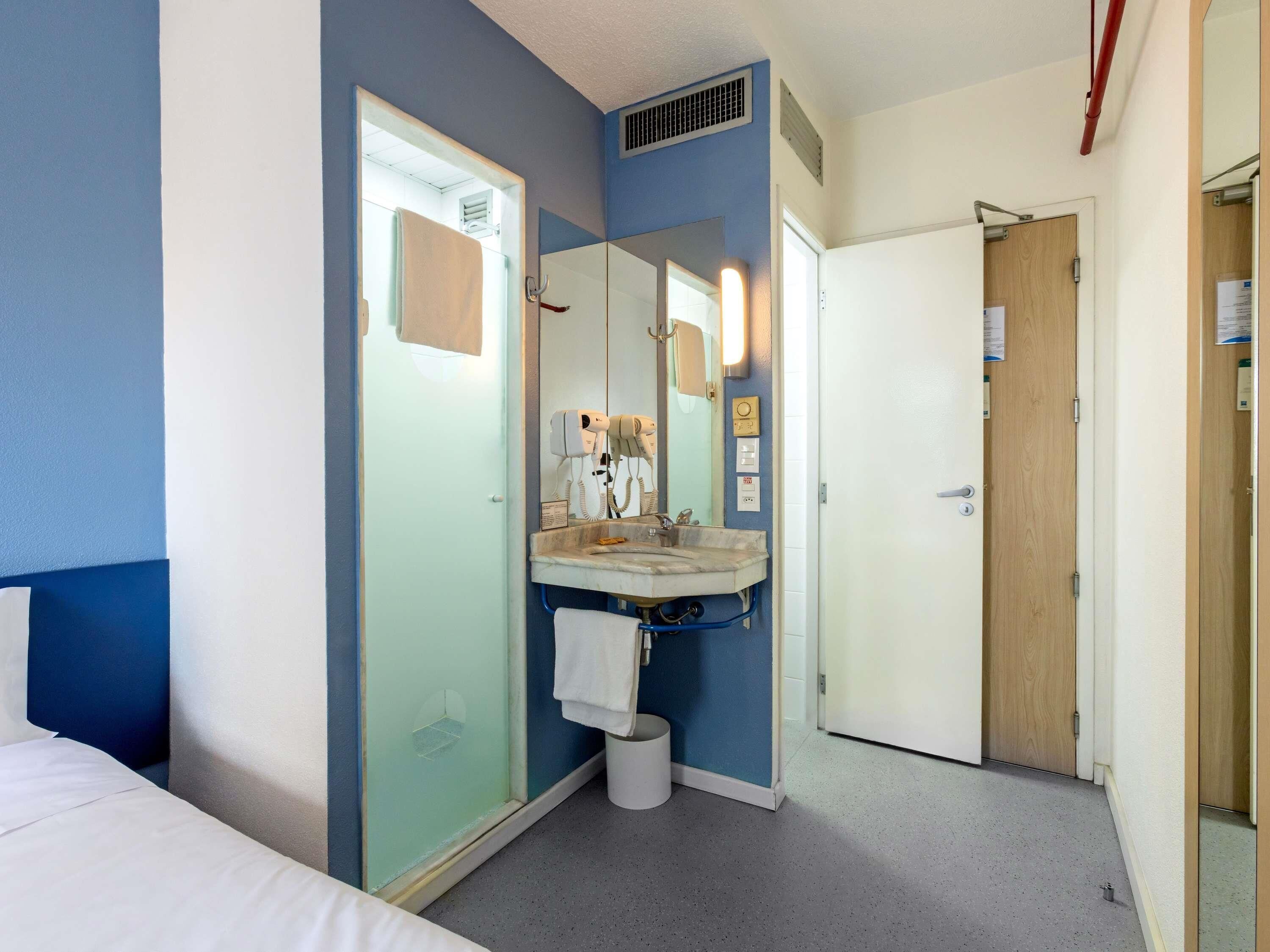 Ein Hotelzimmer mit Bett, Badezimmer inklusive Waschbecken, Spiegel und Föhn sowie einer Tür.