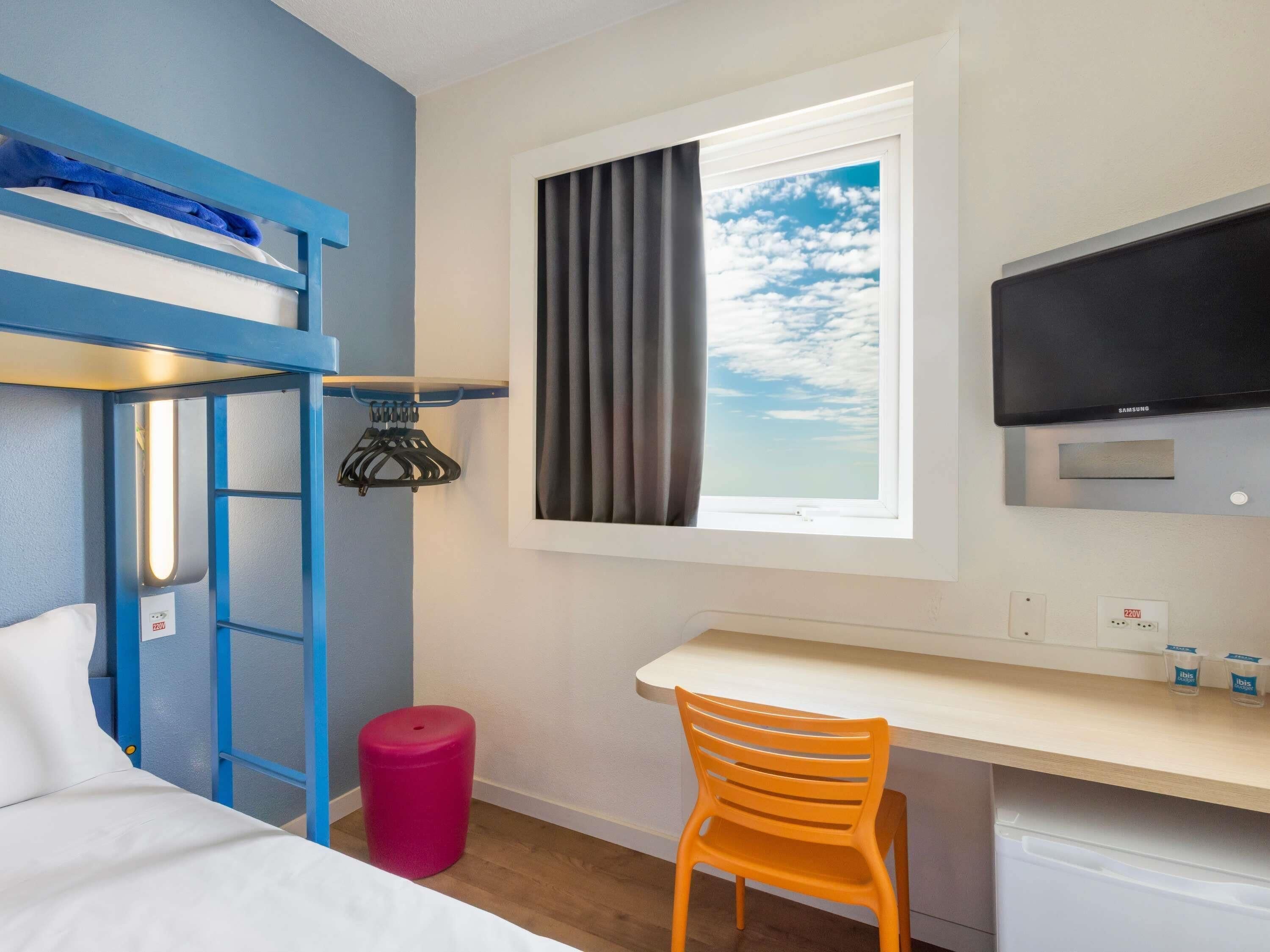 A room with bunk beds, a desk, a chair, a TV, and a window with curtains.