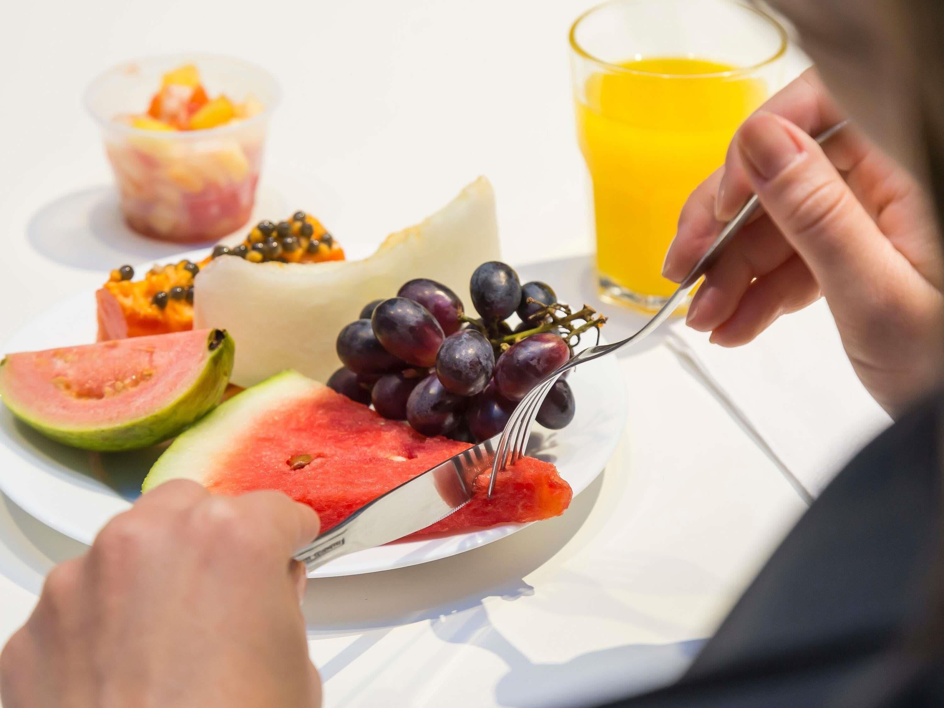 Um prato com melancia, uvas e salada de frutas, um copo de suco de laranja e um garfo.