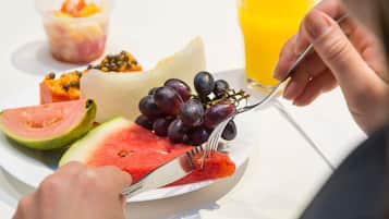 Um prato com melancia, uvas e salada de frutas, um copo de suco de laranja e um garfo.