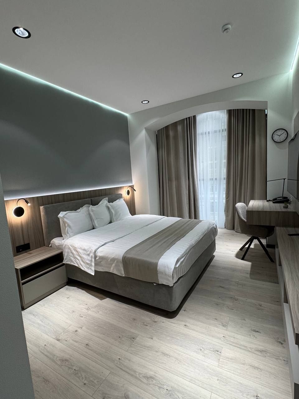 Una camera da letto moderna con un letto grande, comodini, una scrivania e una finestra a forma di arco con tende.