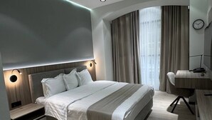 A modern bedroom with a large bed, bedside tables, a desk, and a curved window with curtains. - Asia Grand Hotel (Dushanbe)