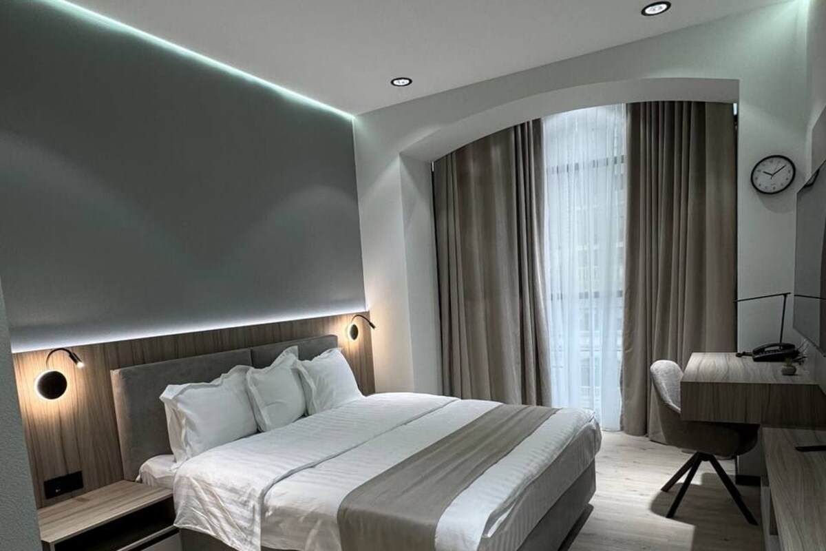 A modern bedroom with a large bed, bedside tables, a desk, and a curved window with curtains.