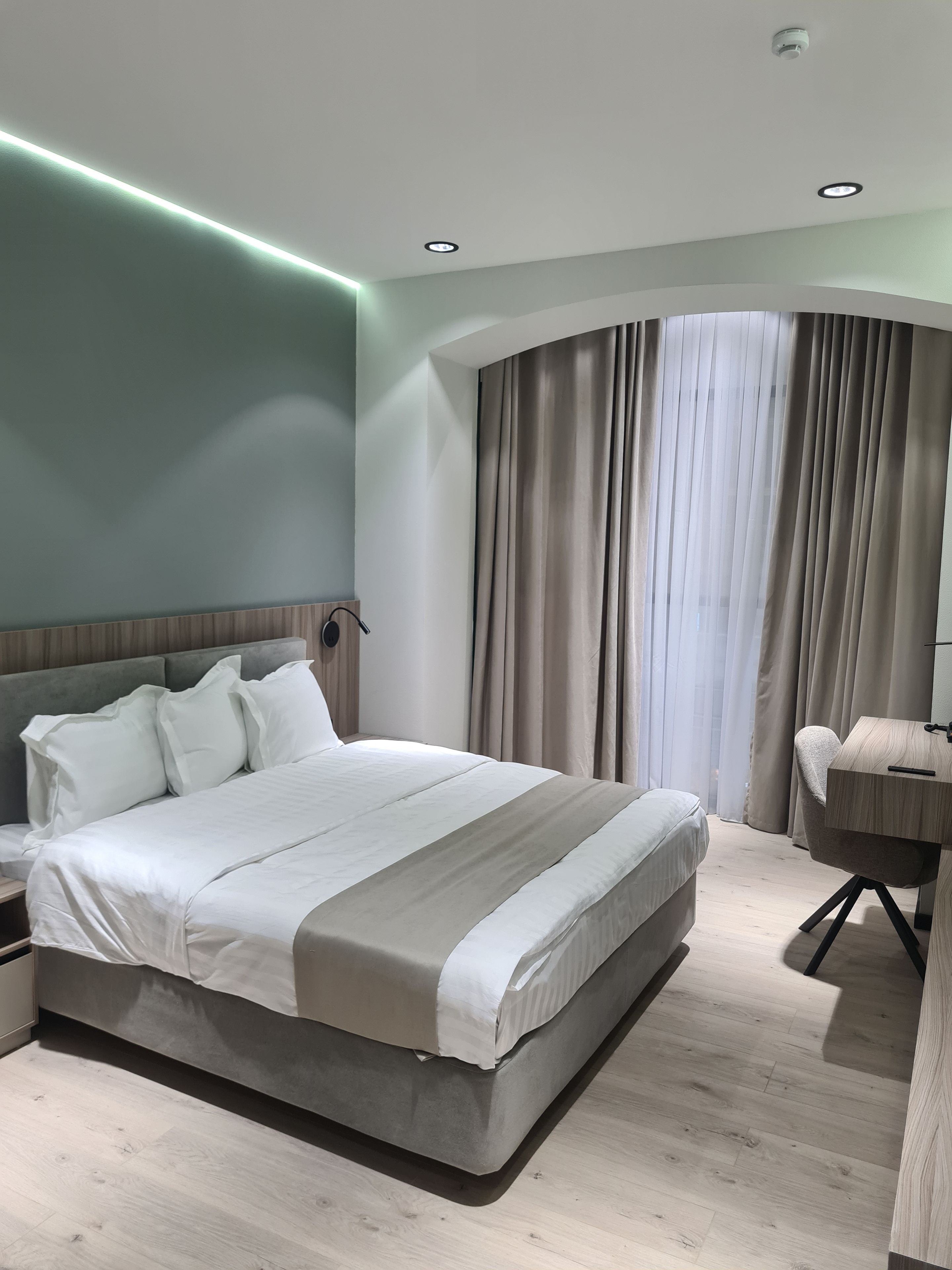 Un dormitorio moderno con una cama grande, un escritorio y un ventanal curvo con cortinas.